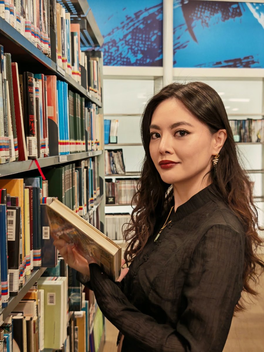 Dr Christine Abigail Tan holding a book among library shelves
